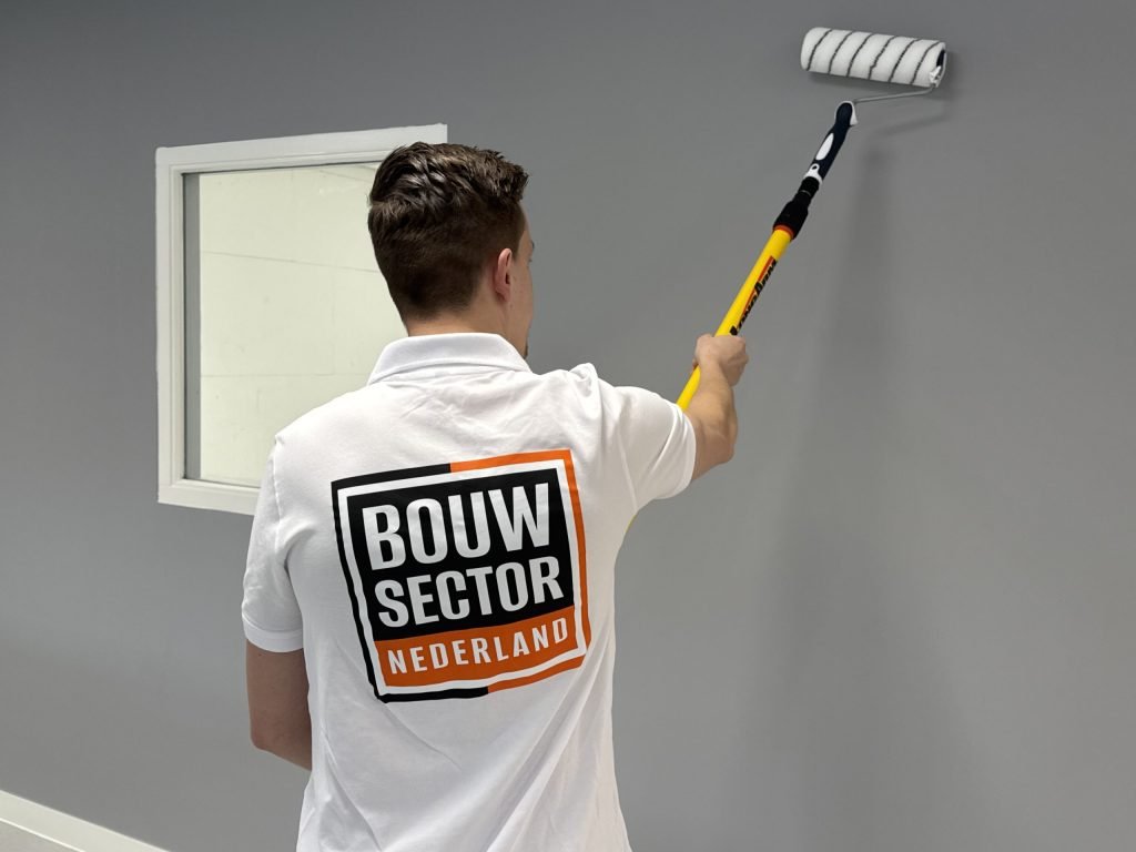Vakman rolt een grijze kleur op een muur naast een raam, van boven naar beneden