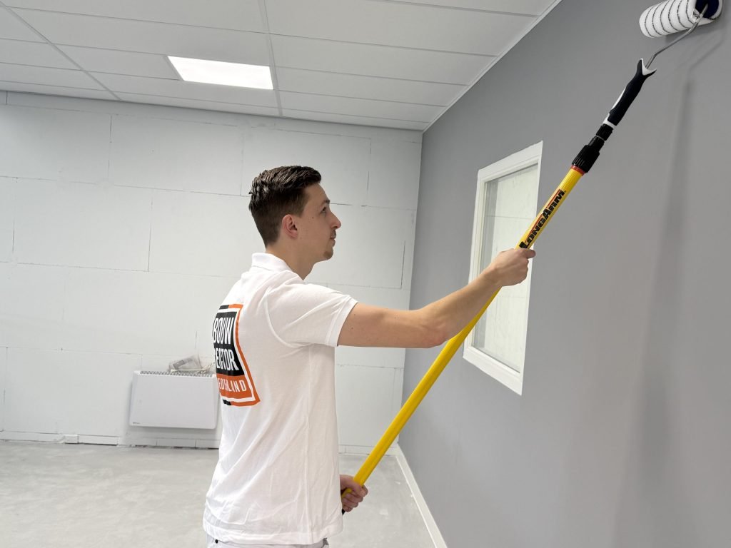 Schilder saust een grijze wand hoog tot aan het systeemplafond met een lange roller