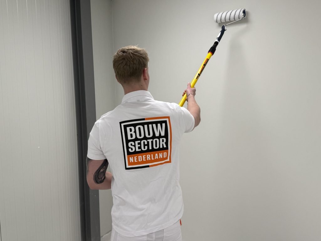 Schilder met getatoeeerde arm rolt verf op een lichte wand in een smalle ruimte