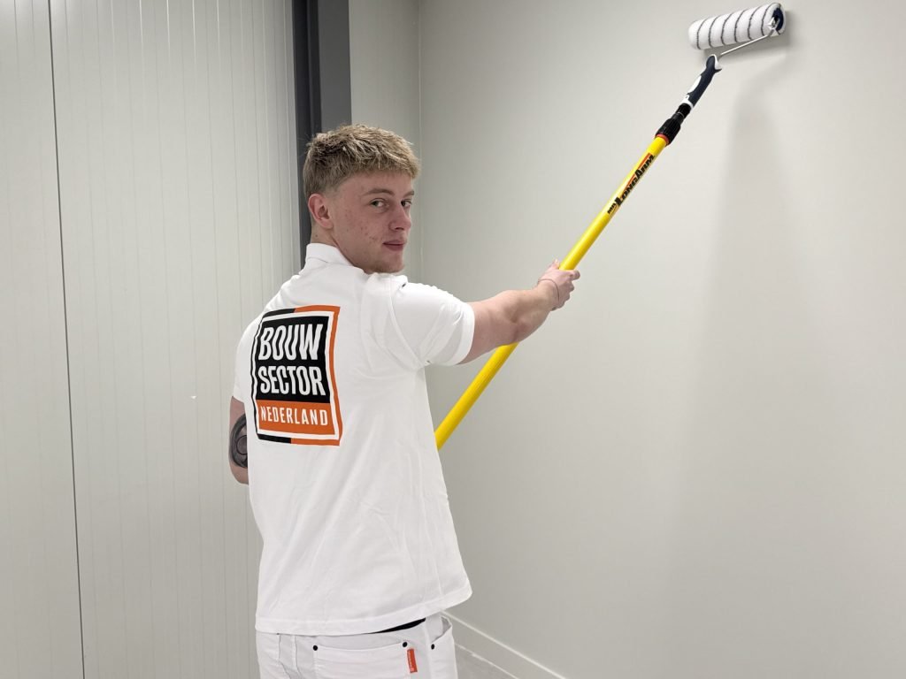 Schilder kijkt over zijn schouder terwijl hij een witte wand met de roller saust