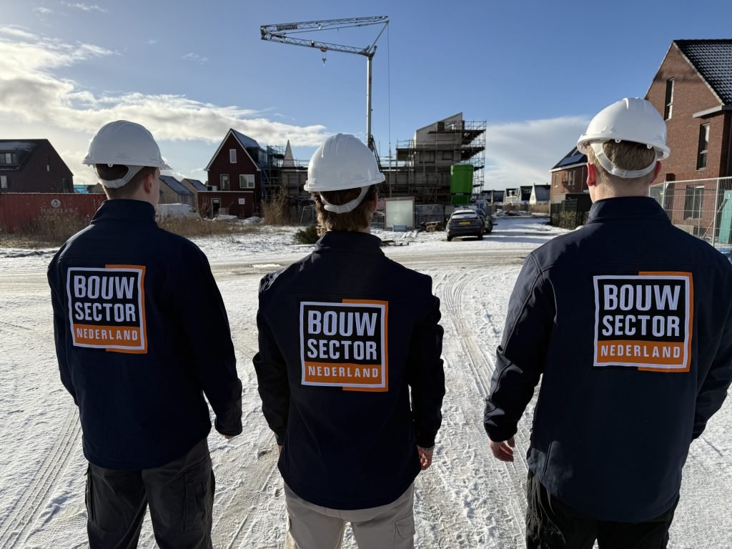 Drie medewerkers van Bouwsector Nederland met witte helm, op de rug gezien, voor nieuwbouwhuizen met een bouwkraan